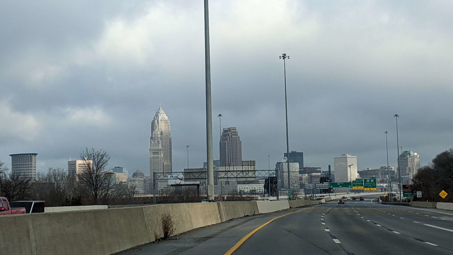 A highway that curved to the right. There is a concrete barricade on the left side. In the background is a city skyline against a dark, cloudy sky.